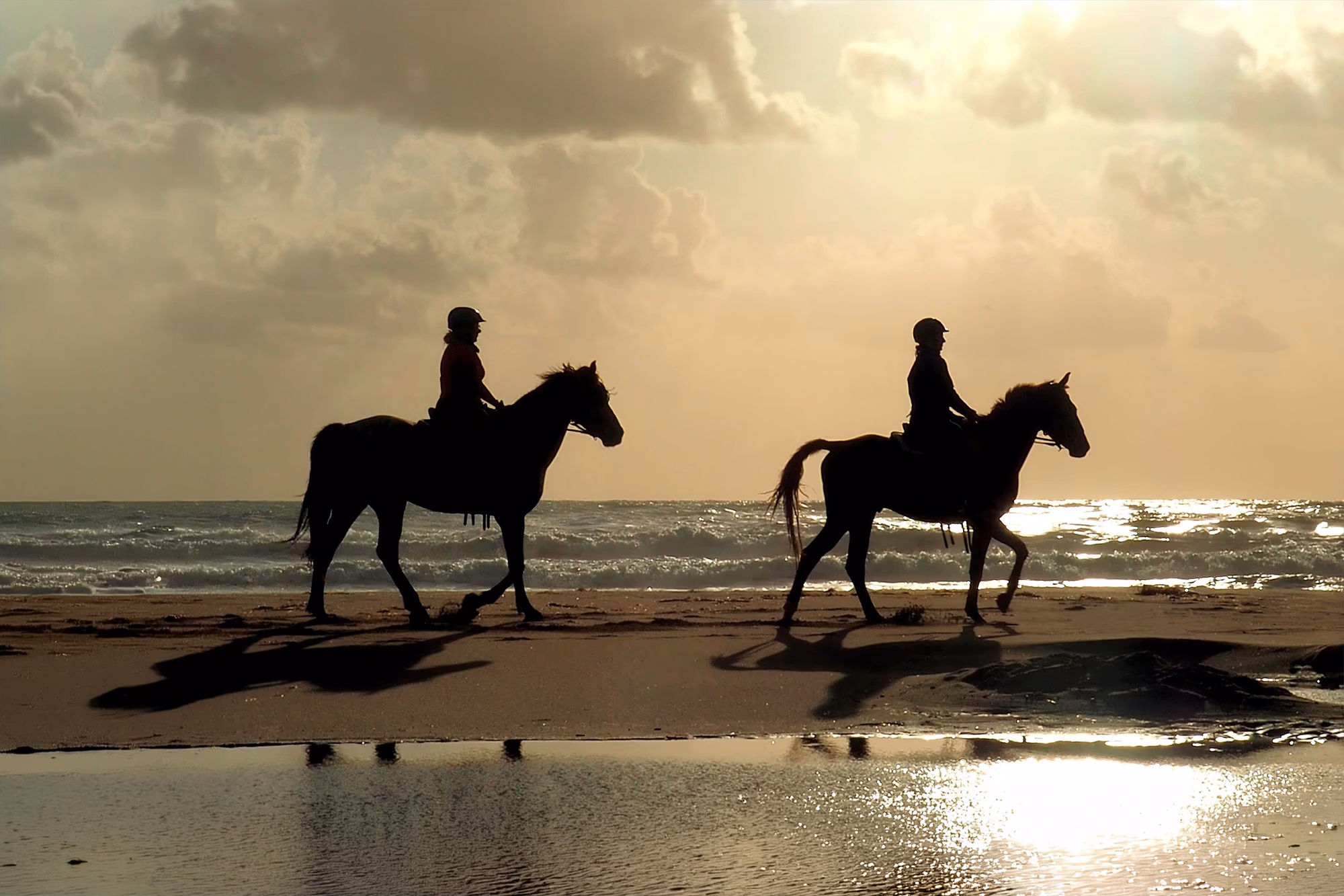 Zwei Reiter an einem Strand bei Sonnenuntergang während eines Reiturlaubs in Spanien.