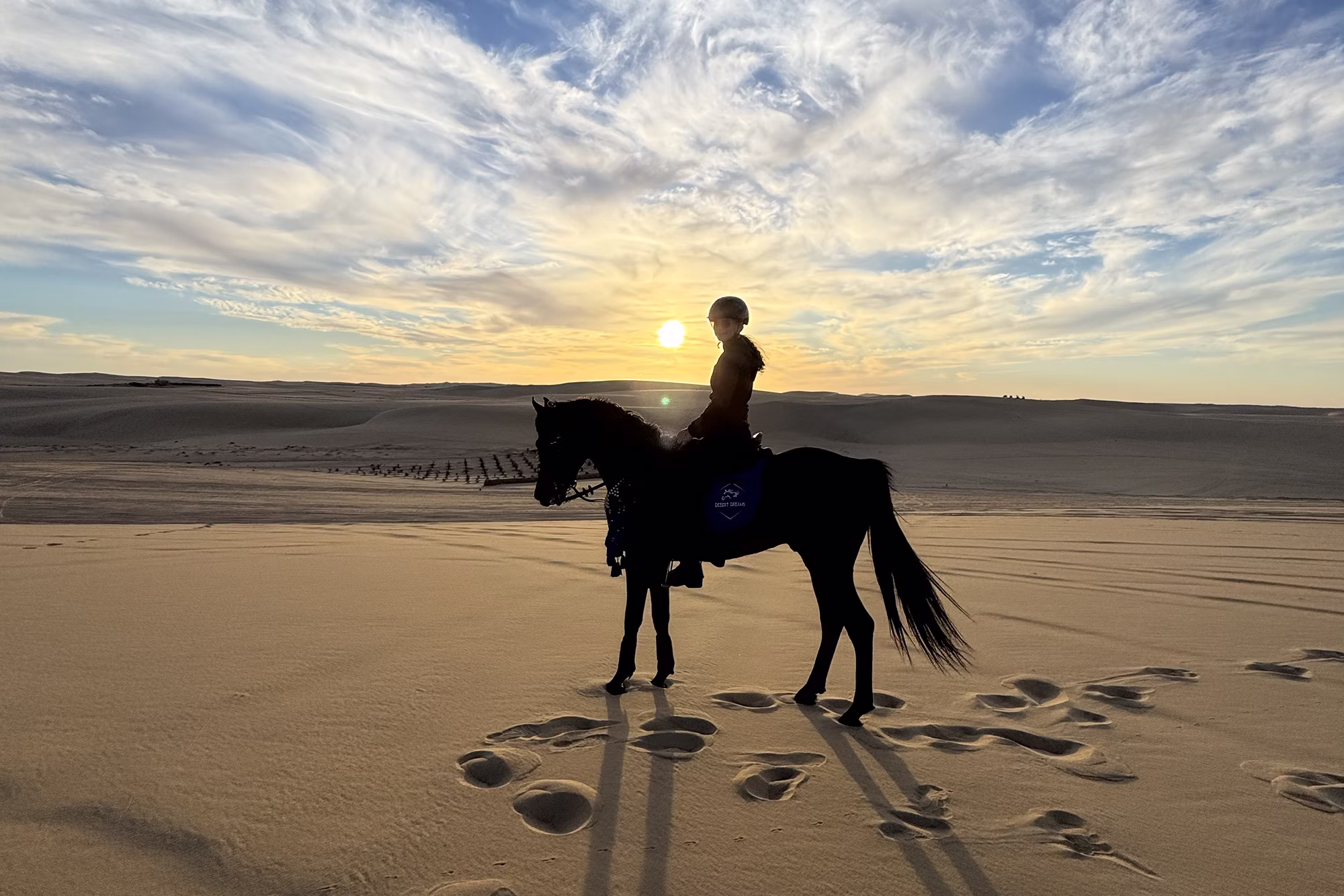 Silhouette einer Reiterin auf einer Sanddüne bei Sonnenuntergang.