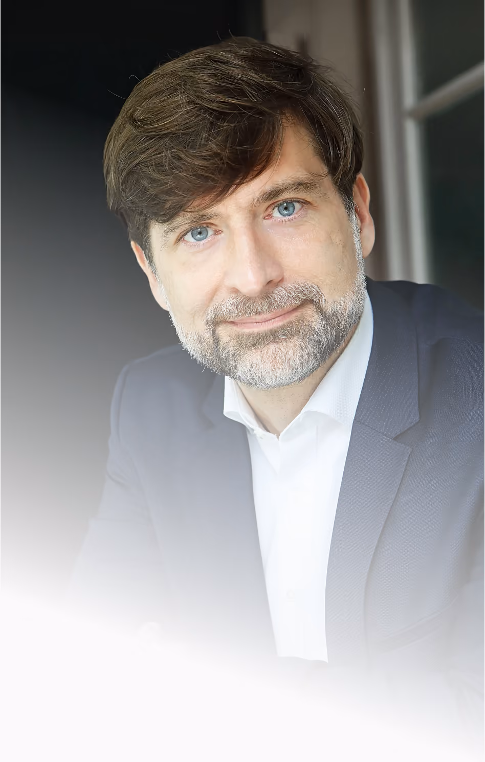 Dr. Peták István with blue eyes, brown hair, and a beard wearing a navy blazer and white shirt, resting his arm on a surface.