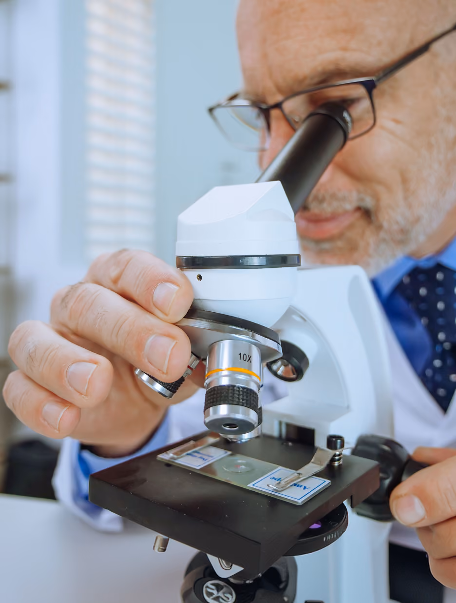 Close-up of a scientist or researcher adjusting the lens of a microscope while looking through the eyepiece in a laboratory setting.