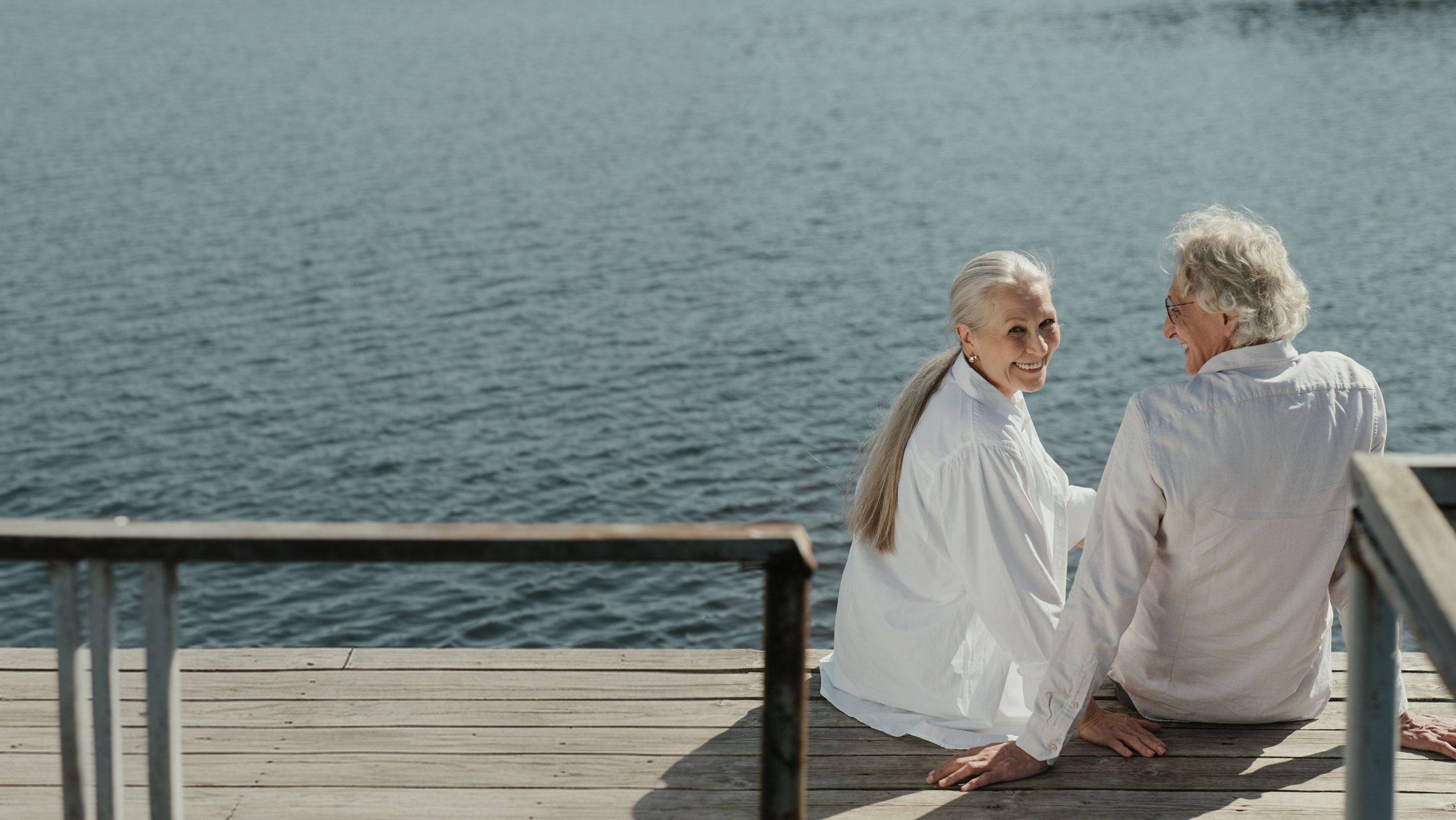 Older couple with gray hair embracing outdoors under clear blue sky, seen from behind.