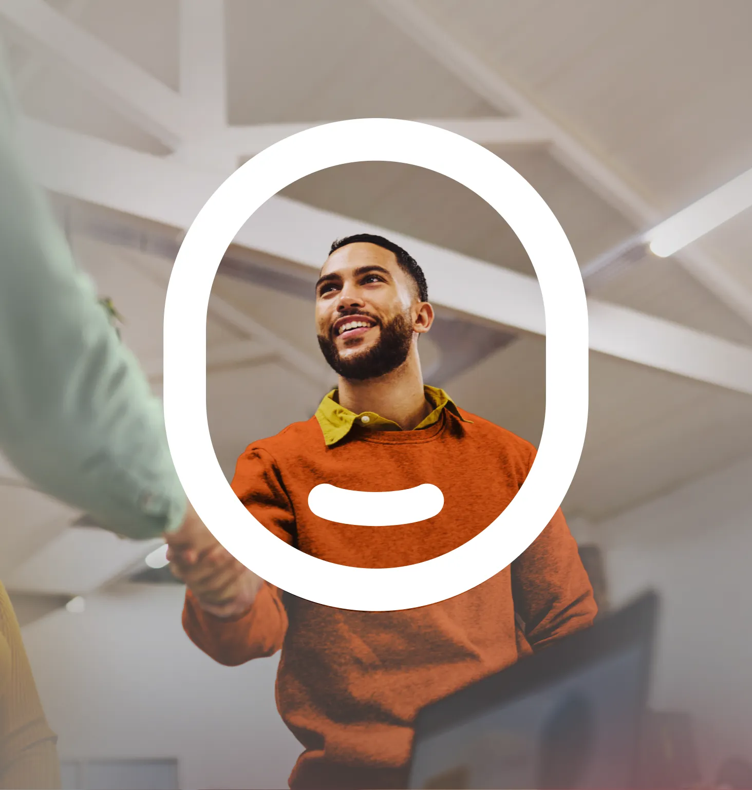 Smiling man in an orange sweater shaking hands, framed by a large white brand logo