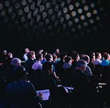 Seated audience in a dimly lit auditorium during a conference talk