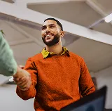 Smiling man in an orange sweater shaking hands with someone in an office