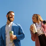 Man and woman laughing together while holding drinks under a blue sky