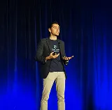 Speaker presenting on stage in front of a blue-lit curtain