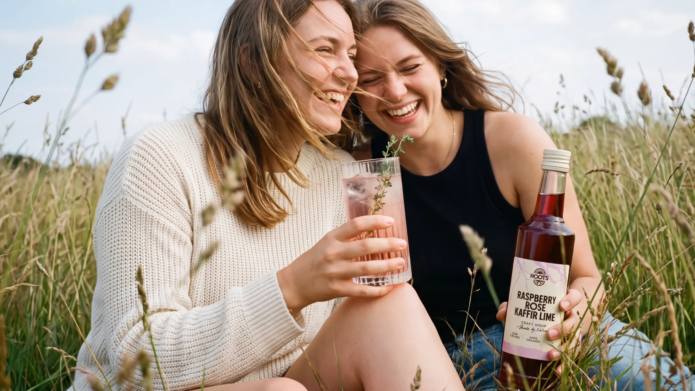 Twee lachende vrouwen in het gras met Roots Raspberry Rose
