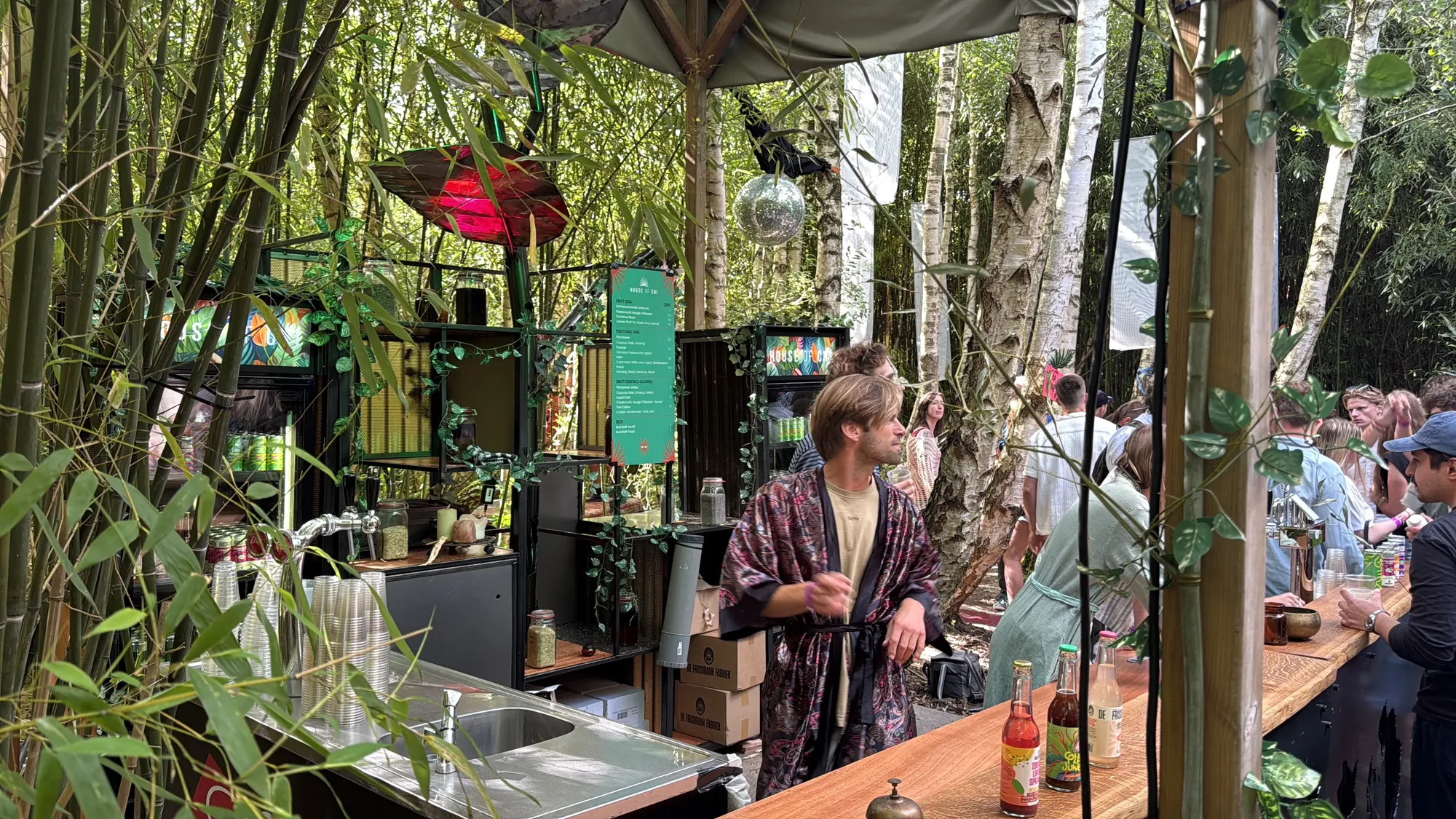 Botanical bar tussen bamboe en planten op een festival, met gasten aan de bar