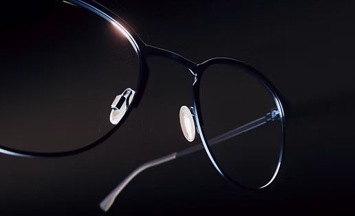 Close-up of black-rimmed eyeglasses with transparent nose pads and thin temples against a dark background.
