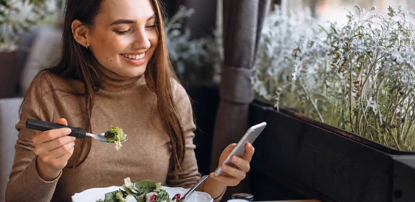 Woman eating a salad while checking the BiteQ app on her phone