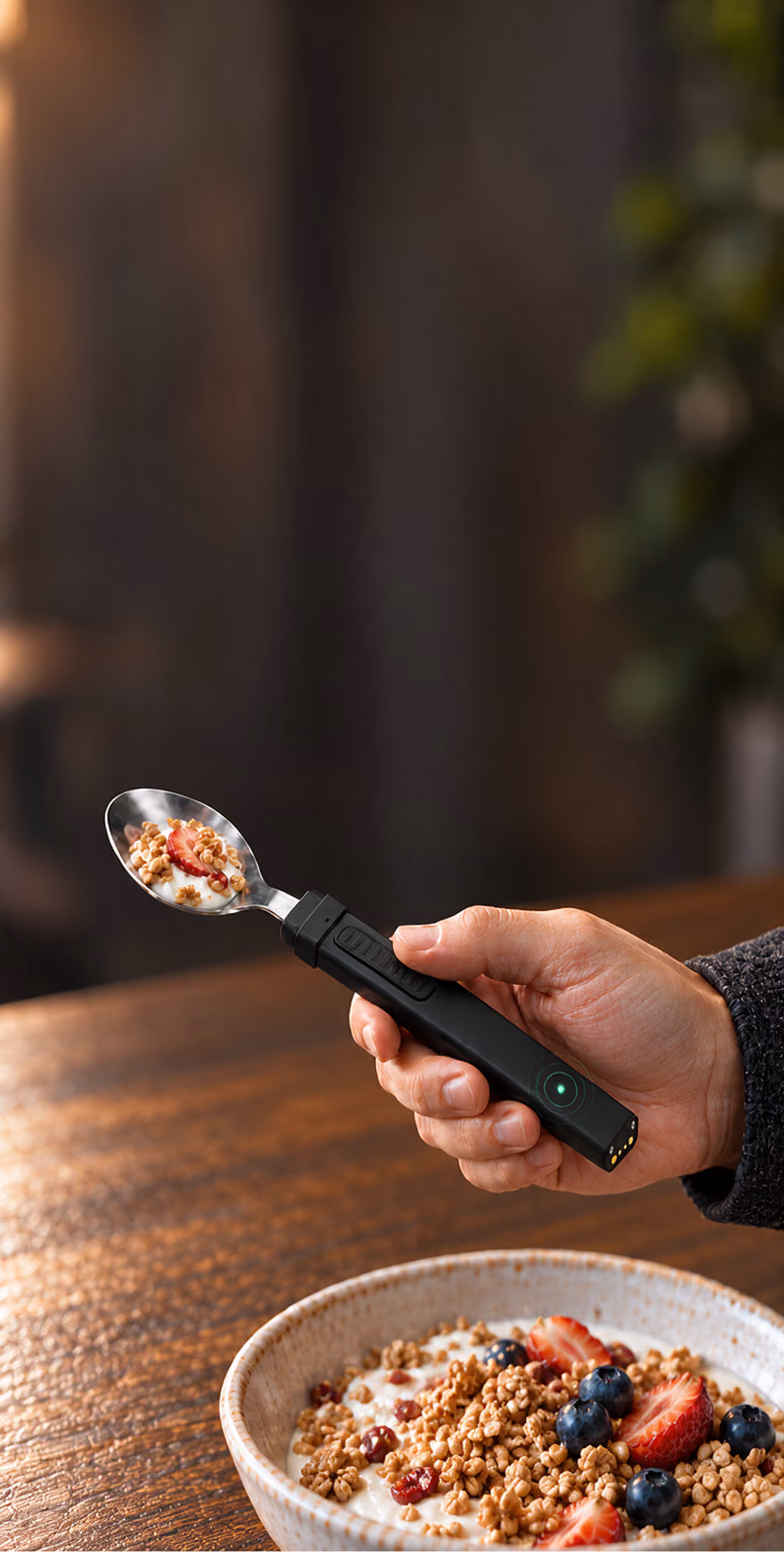 A hand lifting a bite of granola with the BiteQ smart spoon above a breakfast bowl