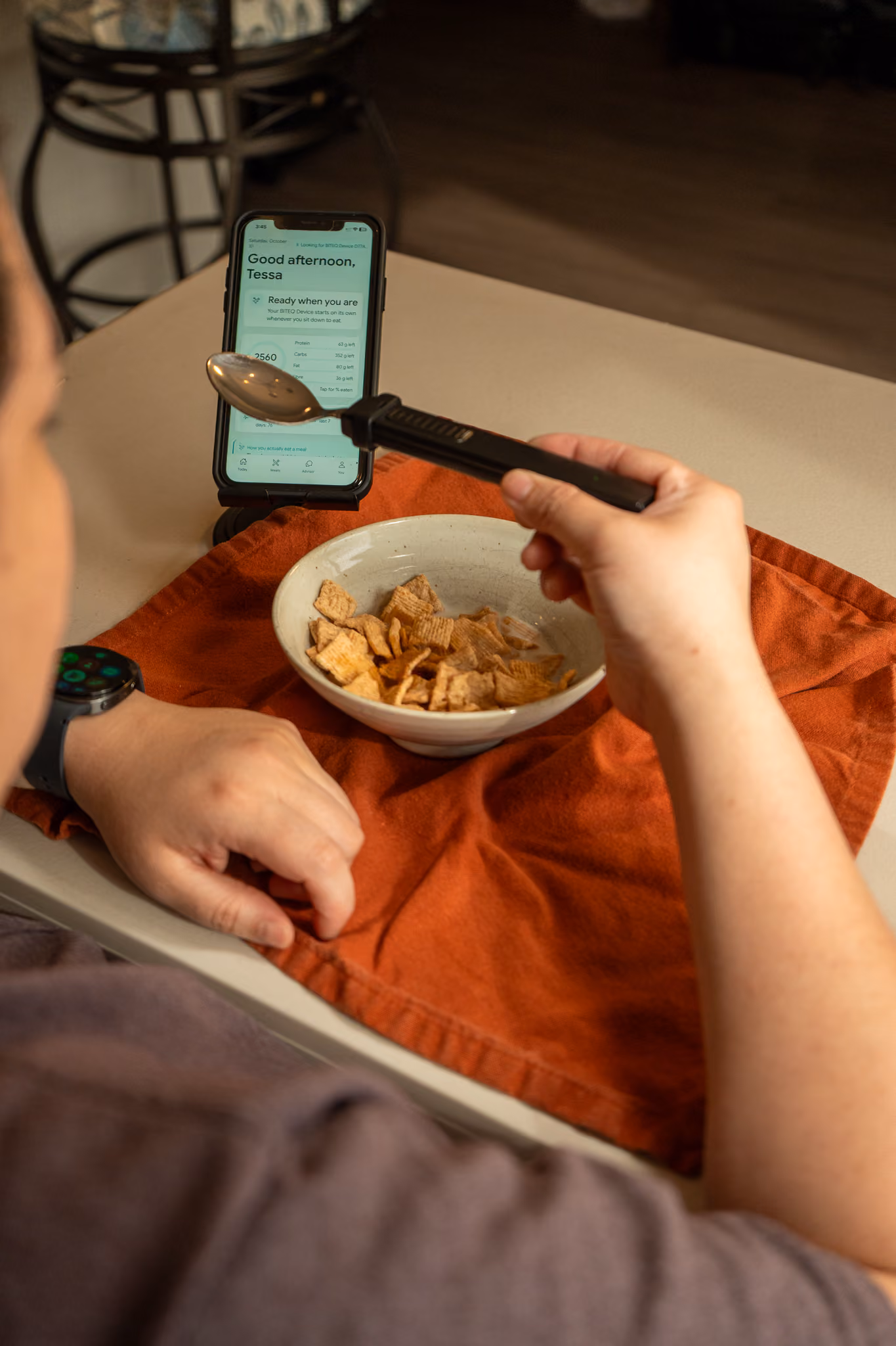 BiteQ utensil held over a plate of food to scan the meal, with a phone on the table