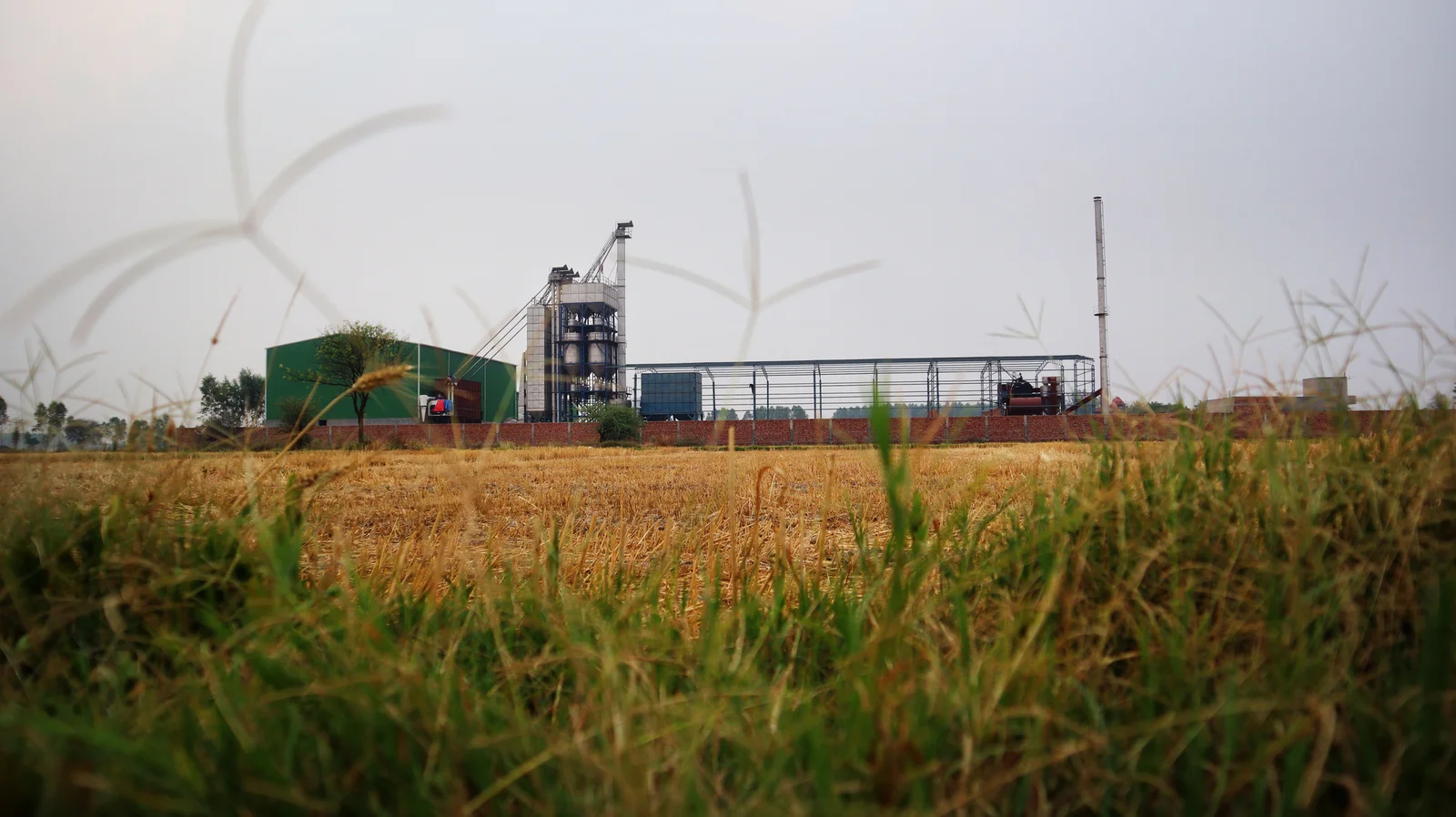 A grain processing and ethanol plant with silos and a chimney, seen across a harvested field