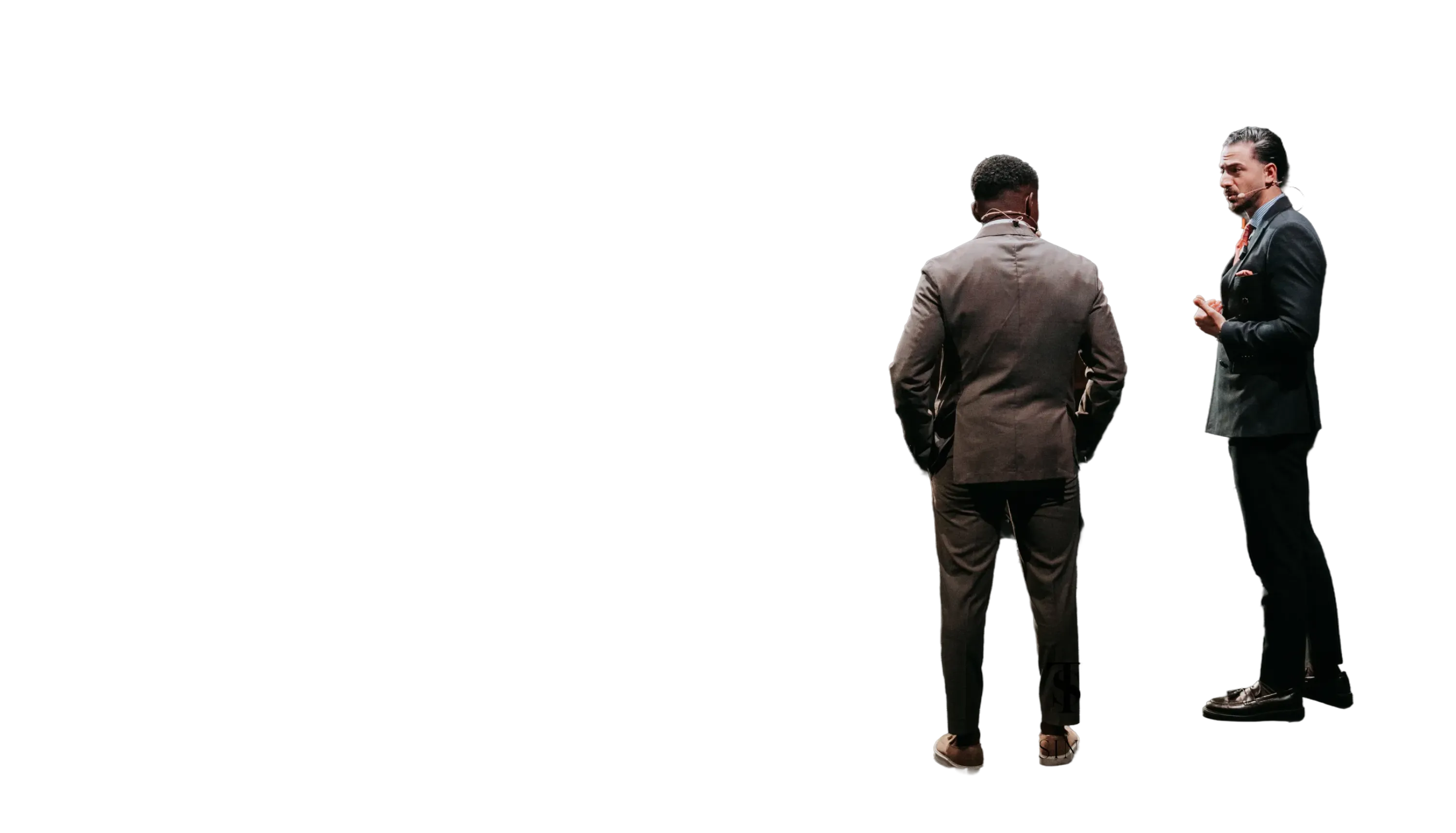 Zwei Männer in Anzügen führen eine Unterhaltung, einer von hinten gesehen, der andere seitlich mit Mikrofon.