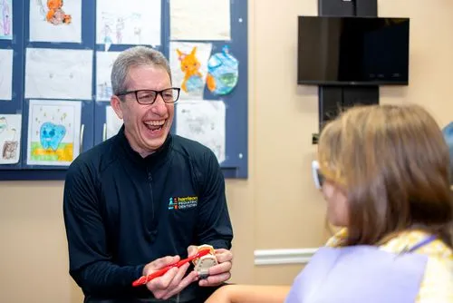 Smiling dentist demonstrating toothbrushing technique on a dental model to a child patient in a colorful dental office.