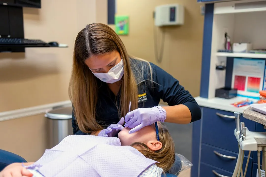 Dentist wearing a mask and gloves examining a child's teeth in a dental clinic.