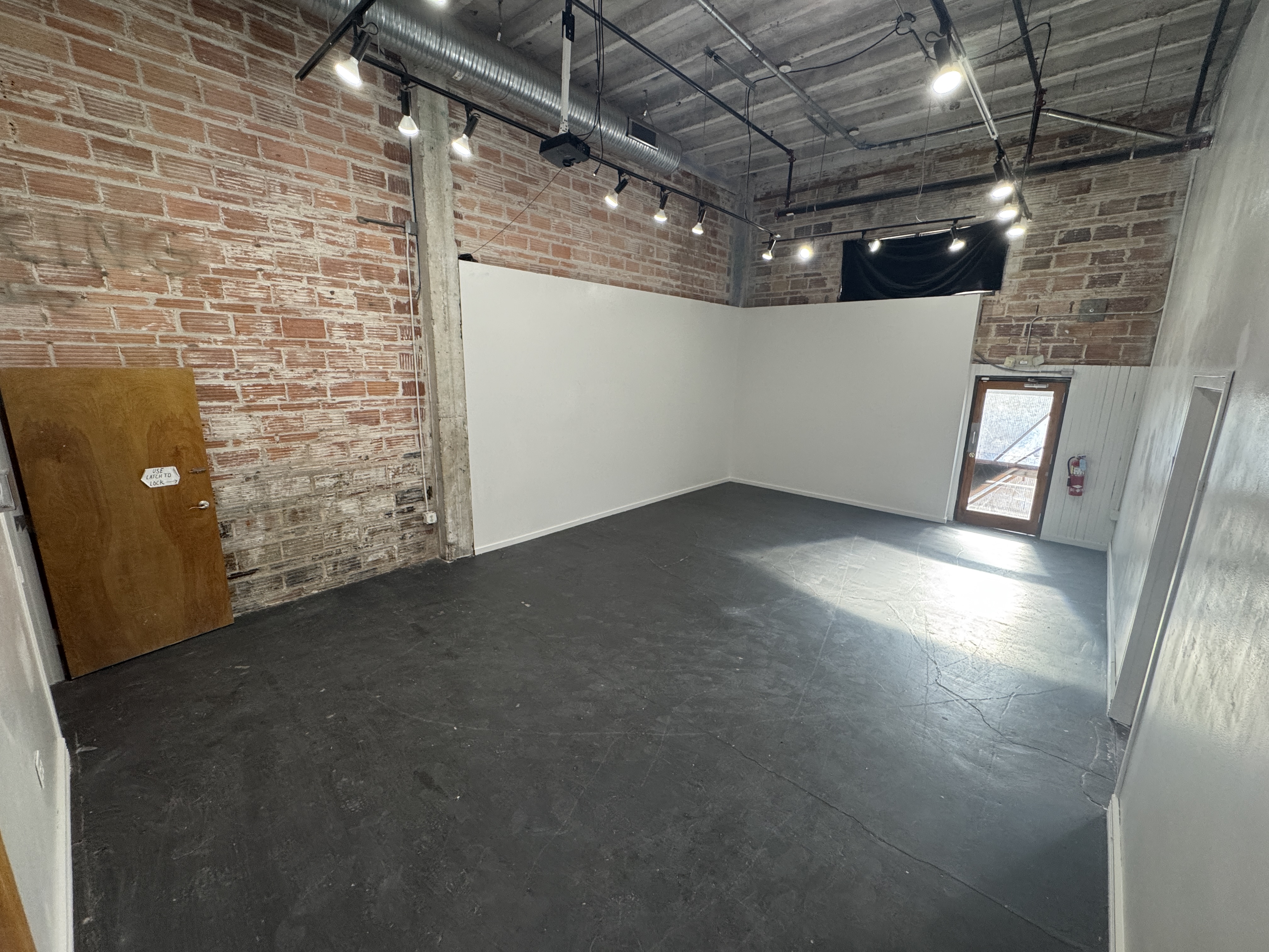 The empty main hall at 108 Blue Star, with exposed brick, white walls and a dark concrete floor