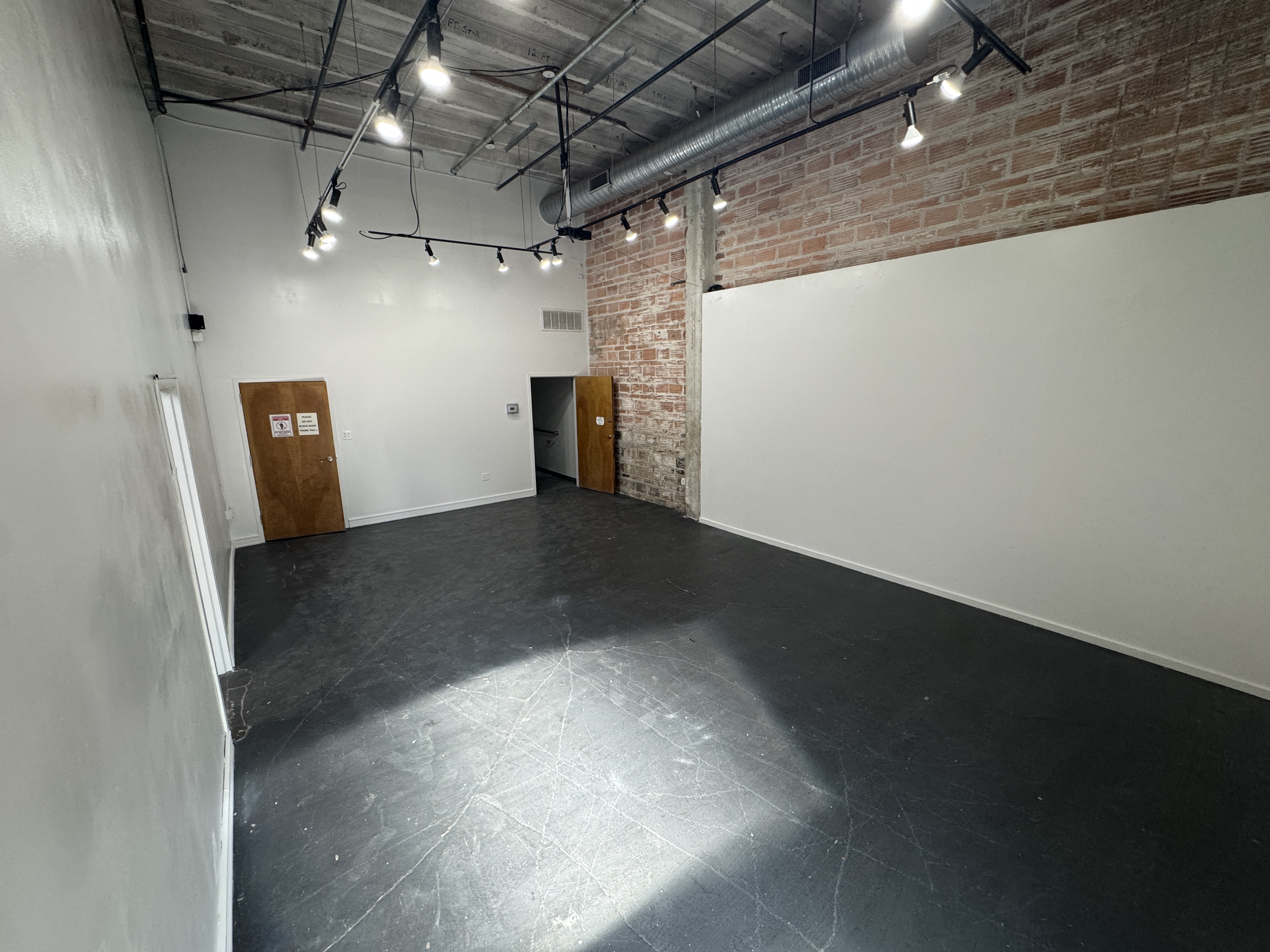 The empty main hall at 108 Blue Star, brick and white walls under track lighting