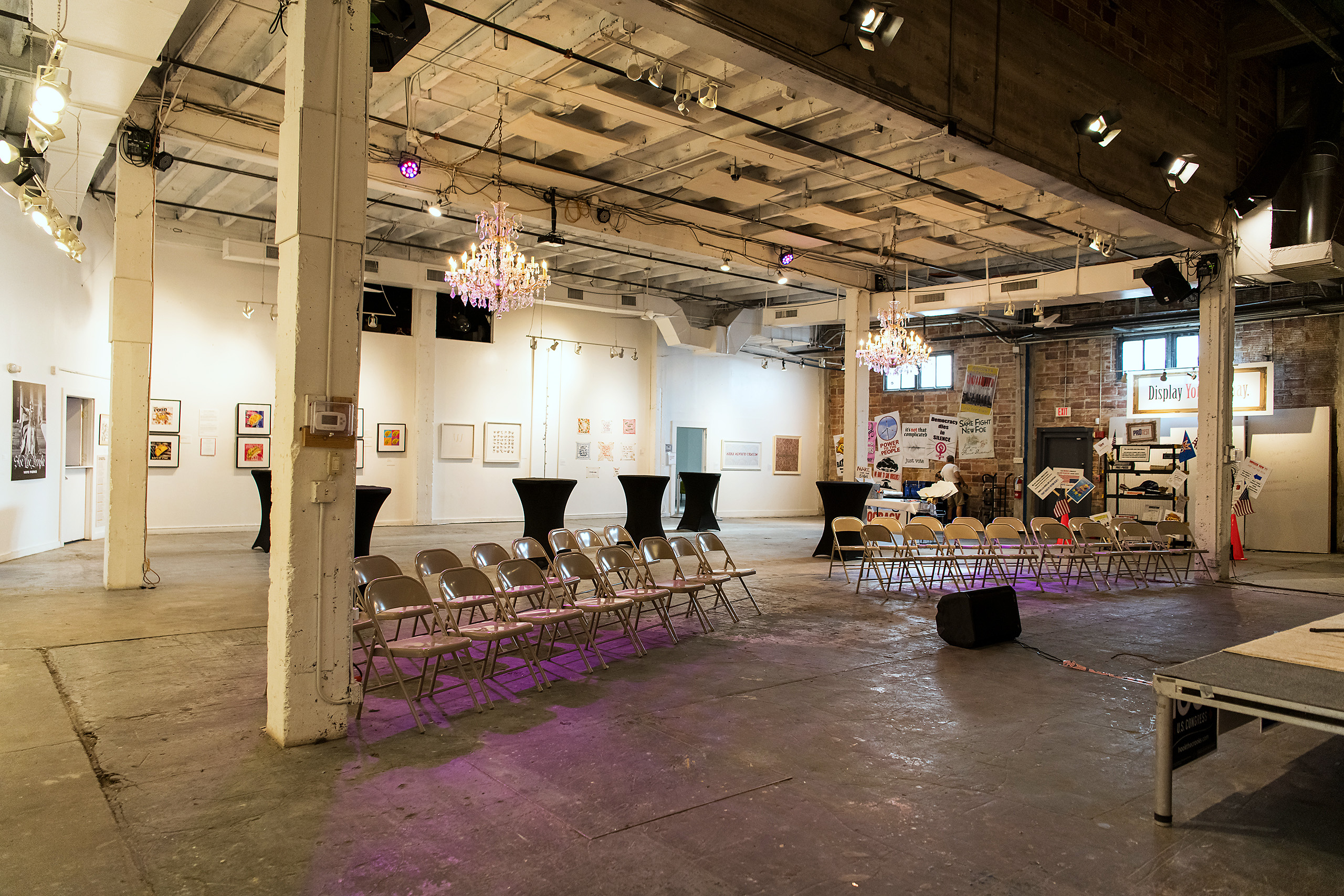 The main hall at 108 Blue Star set with rows of folding chairs for a performance, framed artwork lining the white gallery walls