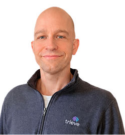 Smiling bald man wearing a navy blue zip-up jacket with the Trieve logo on the left chest, against a white background.