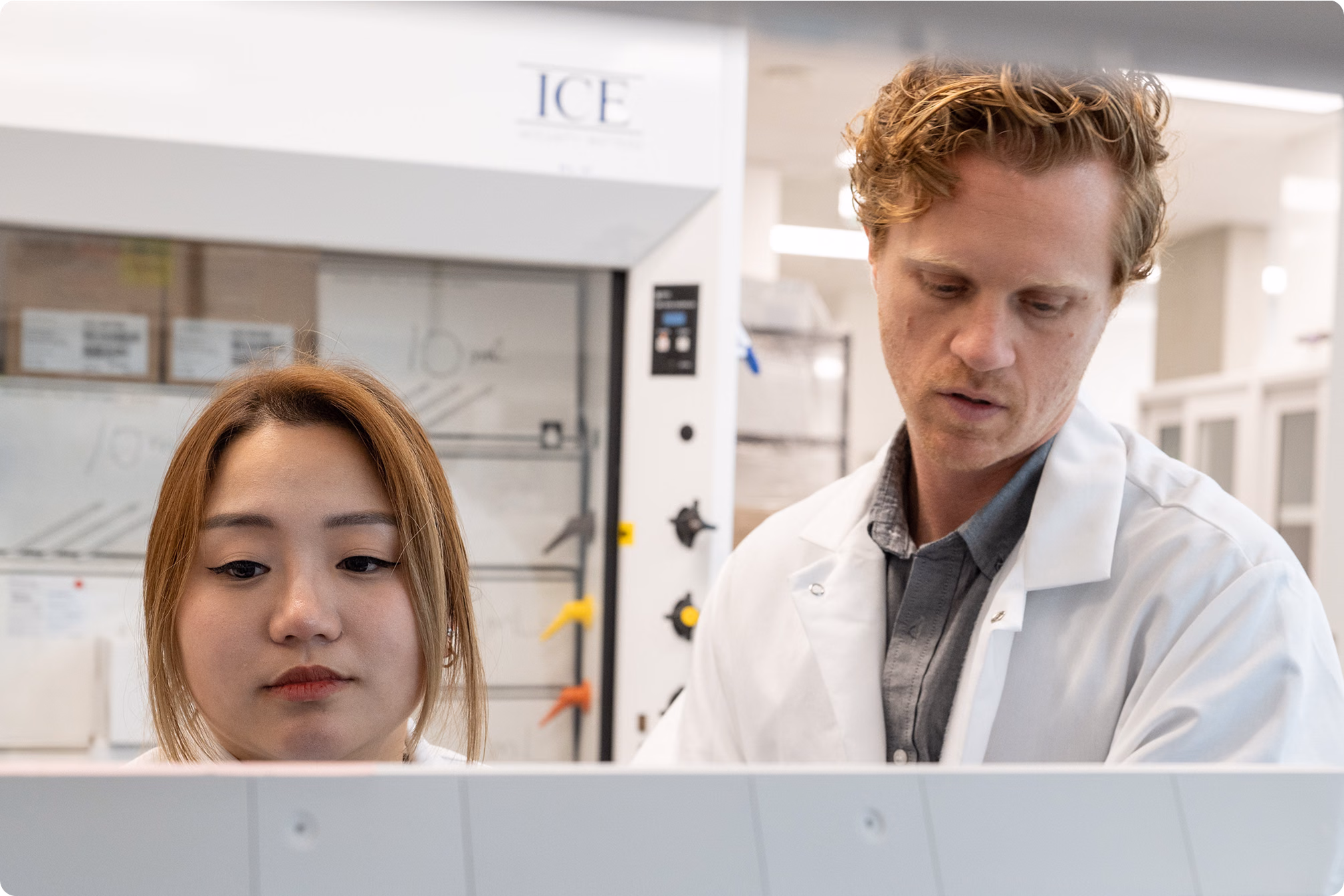 Two scientists wearing white lab coats working together in a laboratory, focusing on an experiment or equipment in front of them.