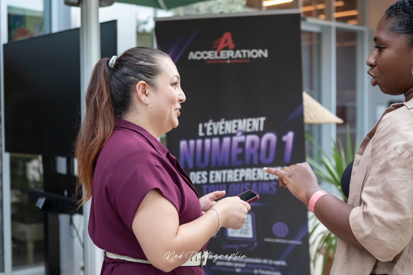 Deux participantes discutent devant le kakémono Accélération, l'événement numéro 1 des entrepreneurs toulousains.