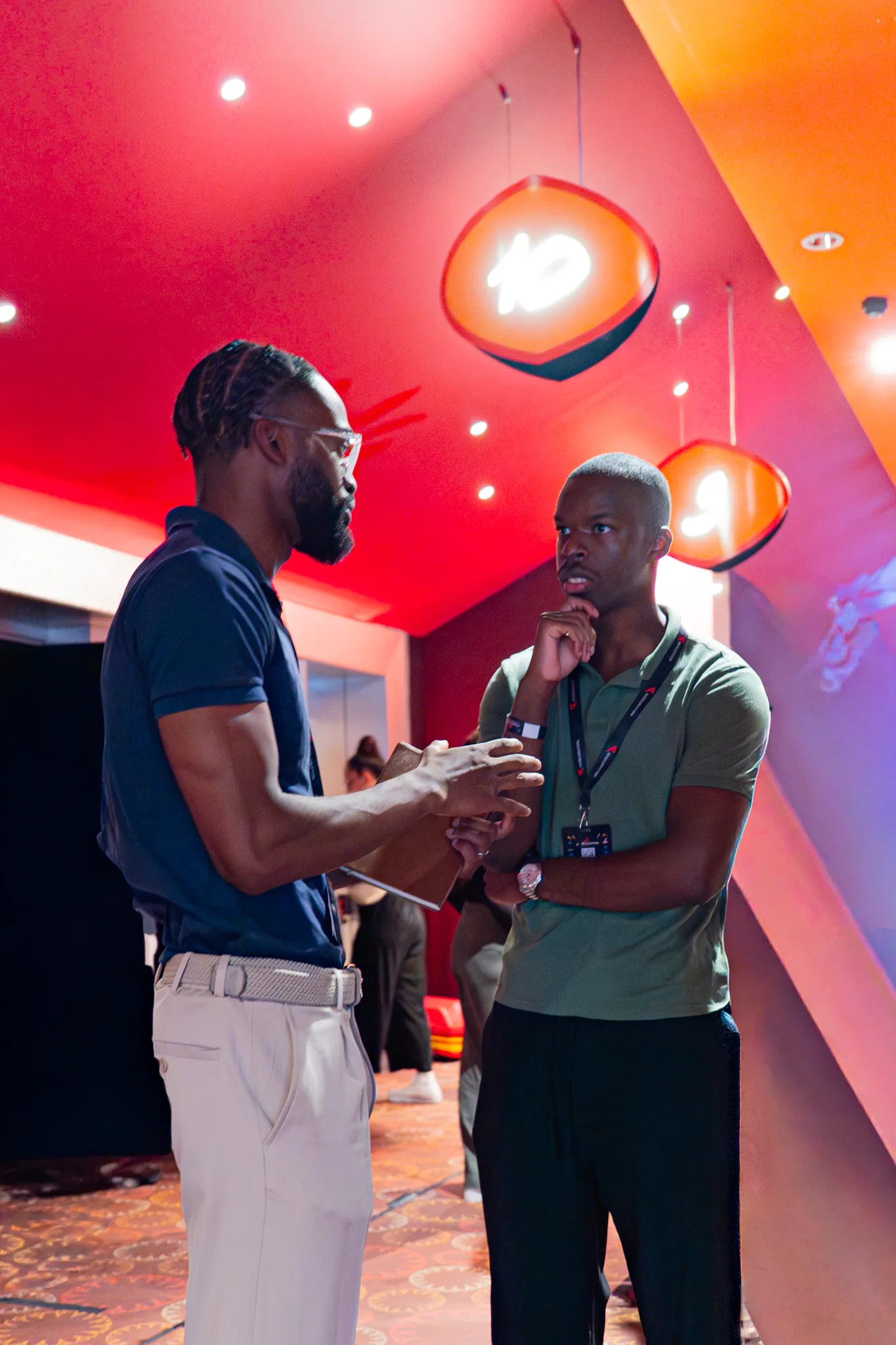 Deux participants en pleine conversation sous l'éclairage rouge et orange de la salle Accélération.