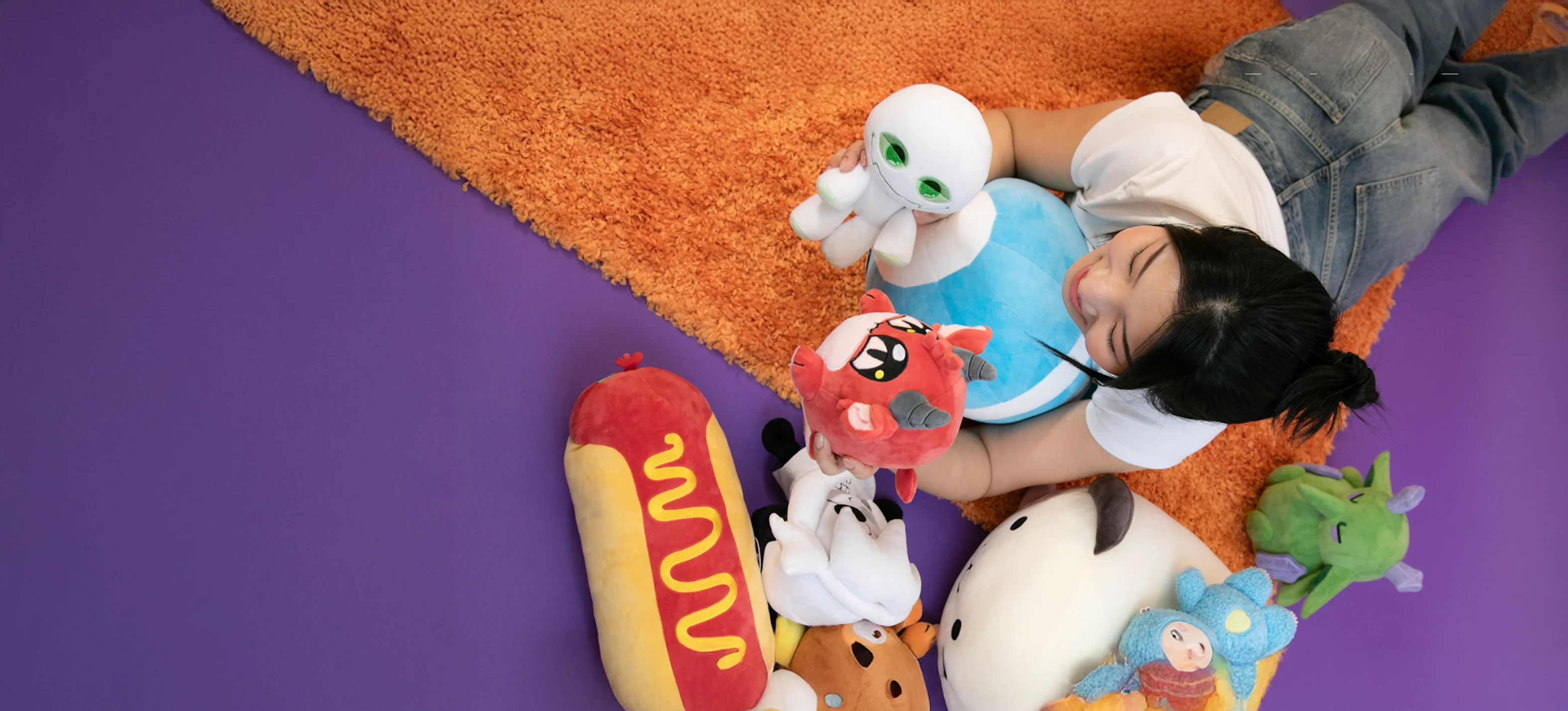 Person lying on an orange rug with several colorful plush toys including a green alien, red creature, hot dog, and other cartoon characters on a purple floor.