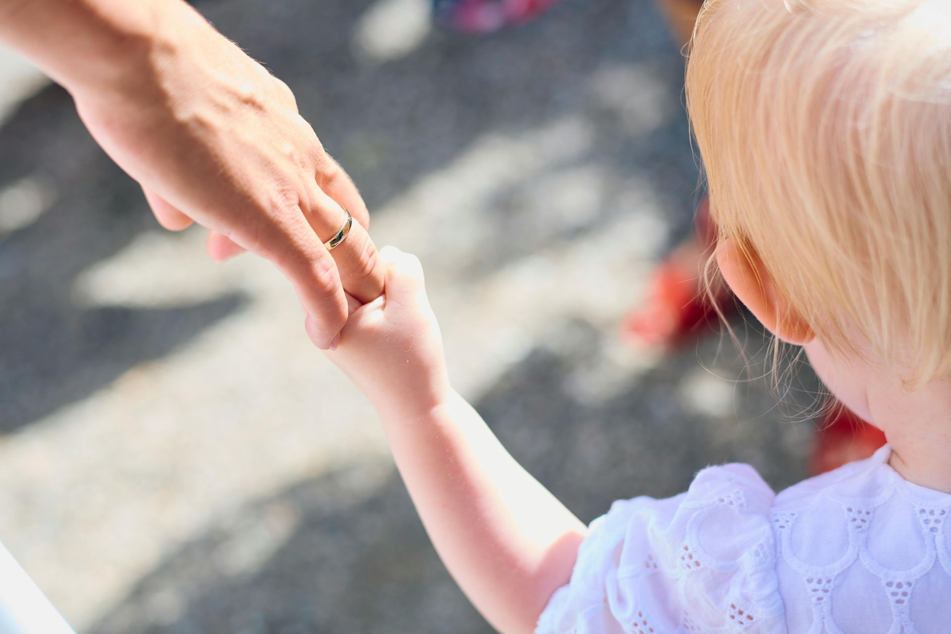 Adult holding a young child’s hand outdoors in bright sunlight