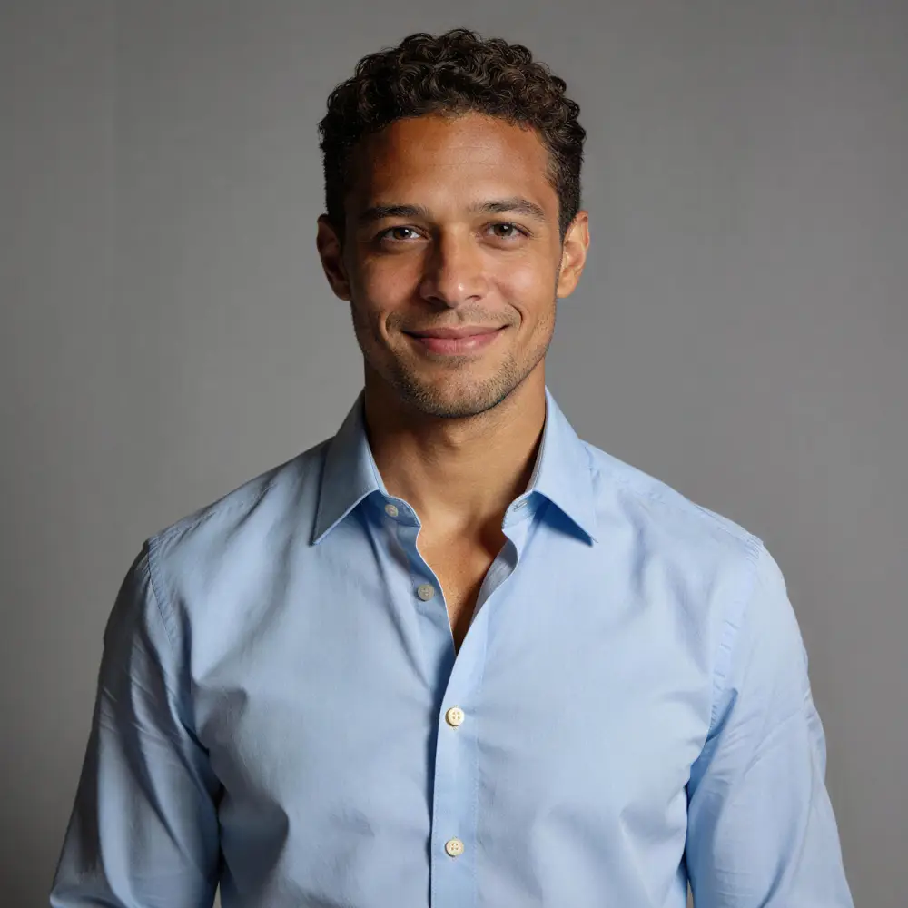 Smiling man with curly hair wearing a light blue button-up shirt against a gray background.