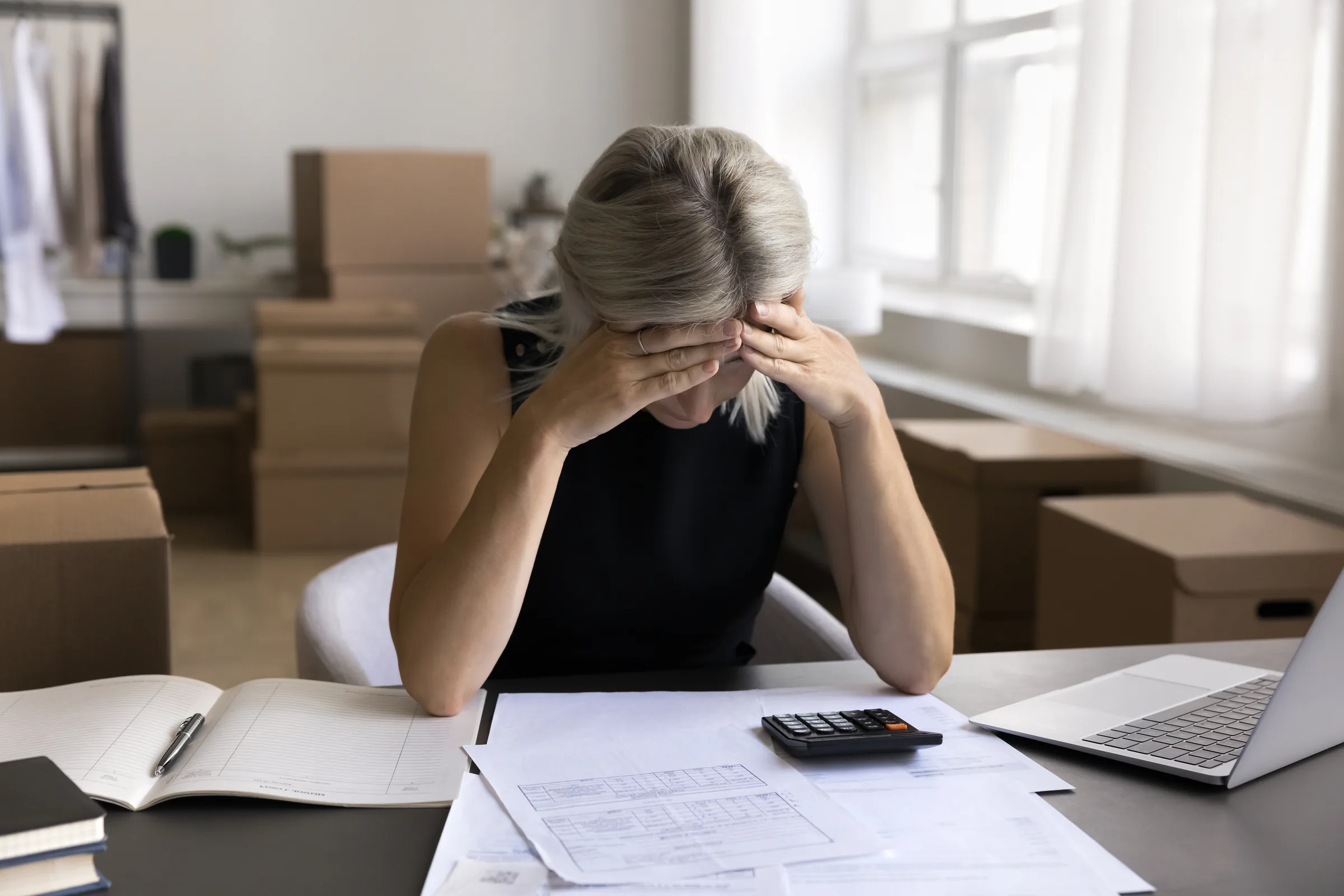 Woman with her head in her hands reviewing overdue bills at a kitchen table