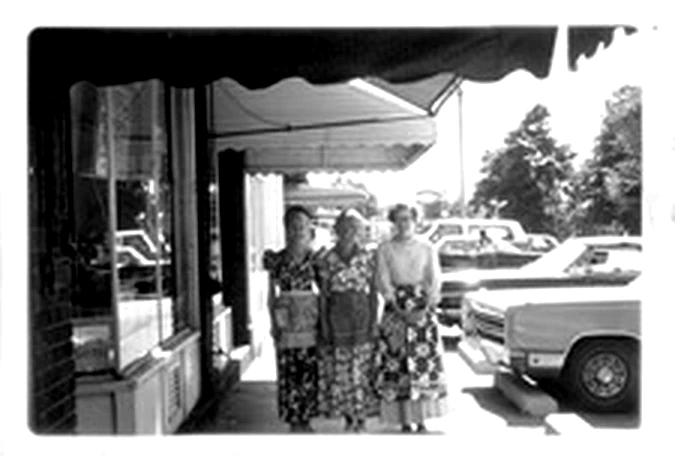 Customers standing outside the bakery windows on Olde 8 Road, cars parked at the kerb