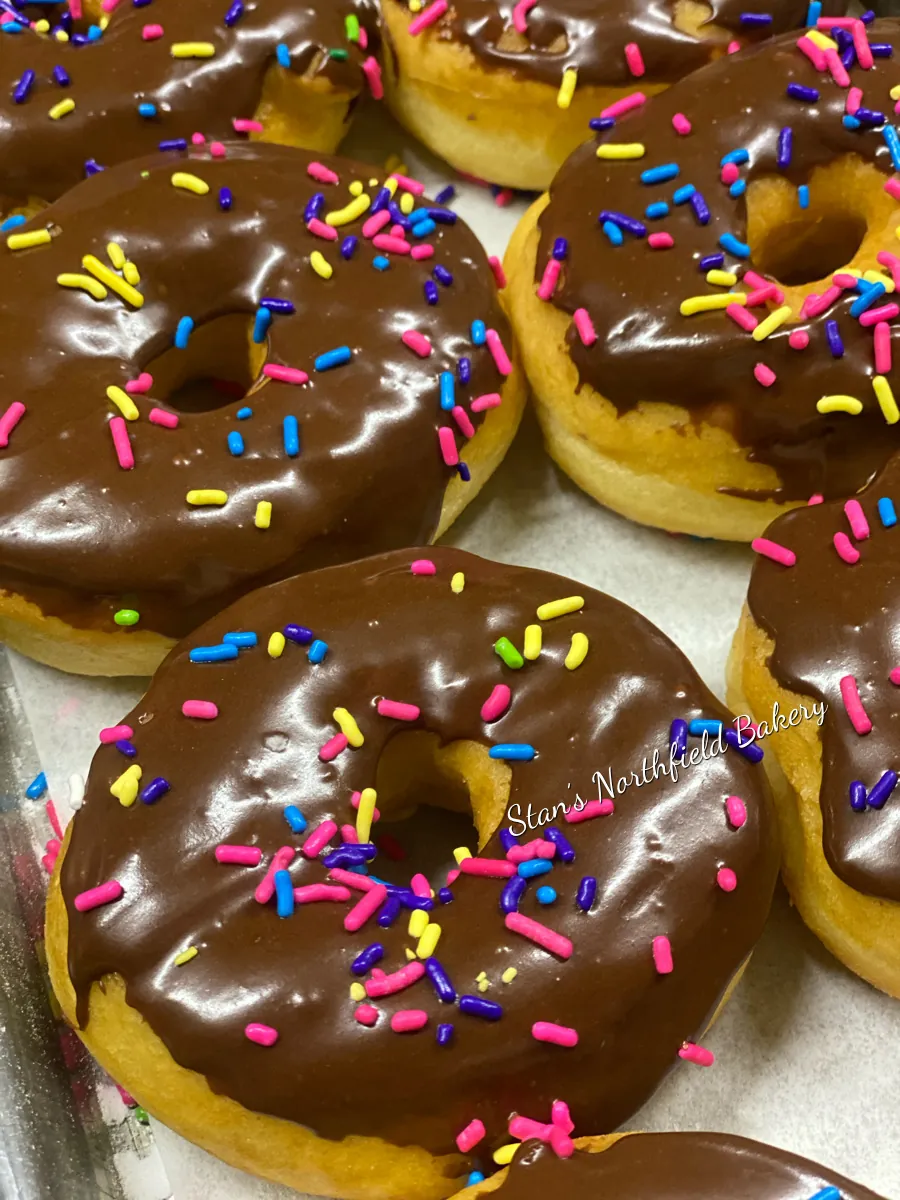 Chocolate-glazed donuts with rainbow sprinkles on a bakery tray