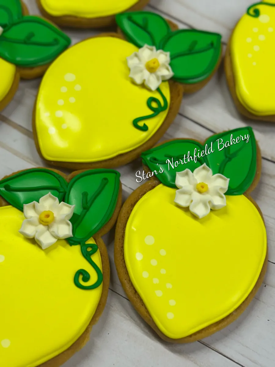 Lemon-shaped sugar cookies in yellow royal icing with green leaves and white flowers