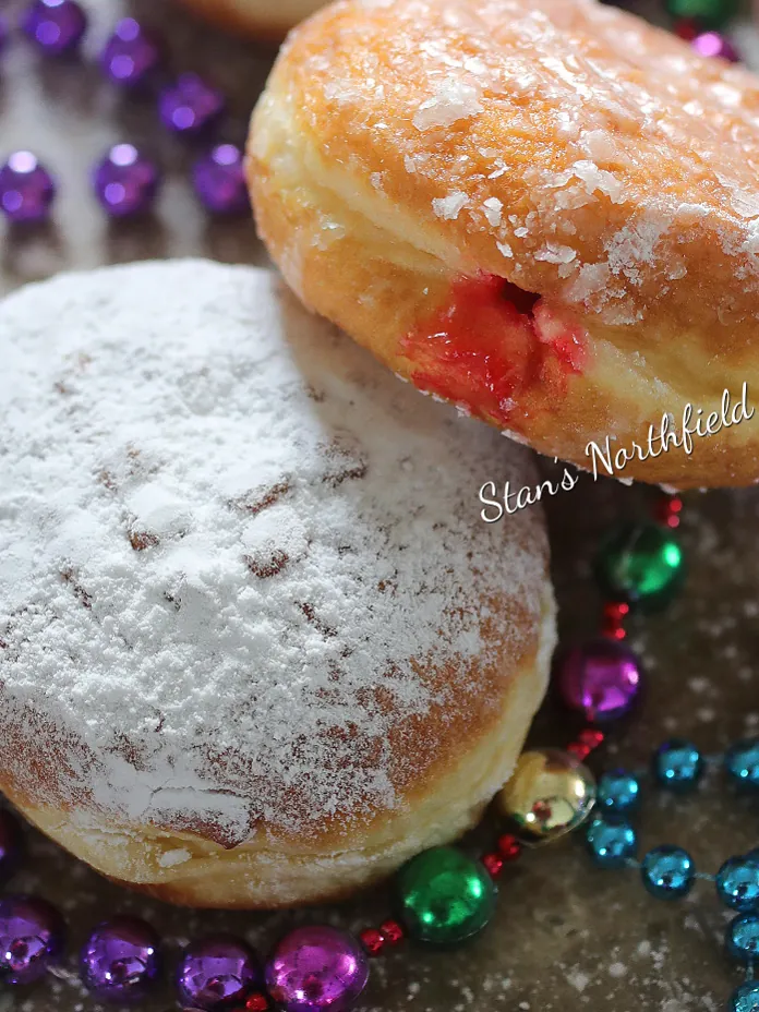 Powdered and glazed pączki with raspberry filling on Mardi Gras beads