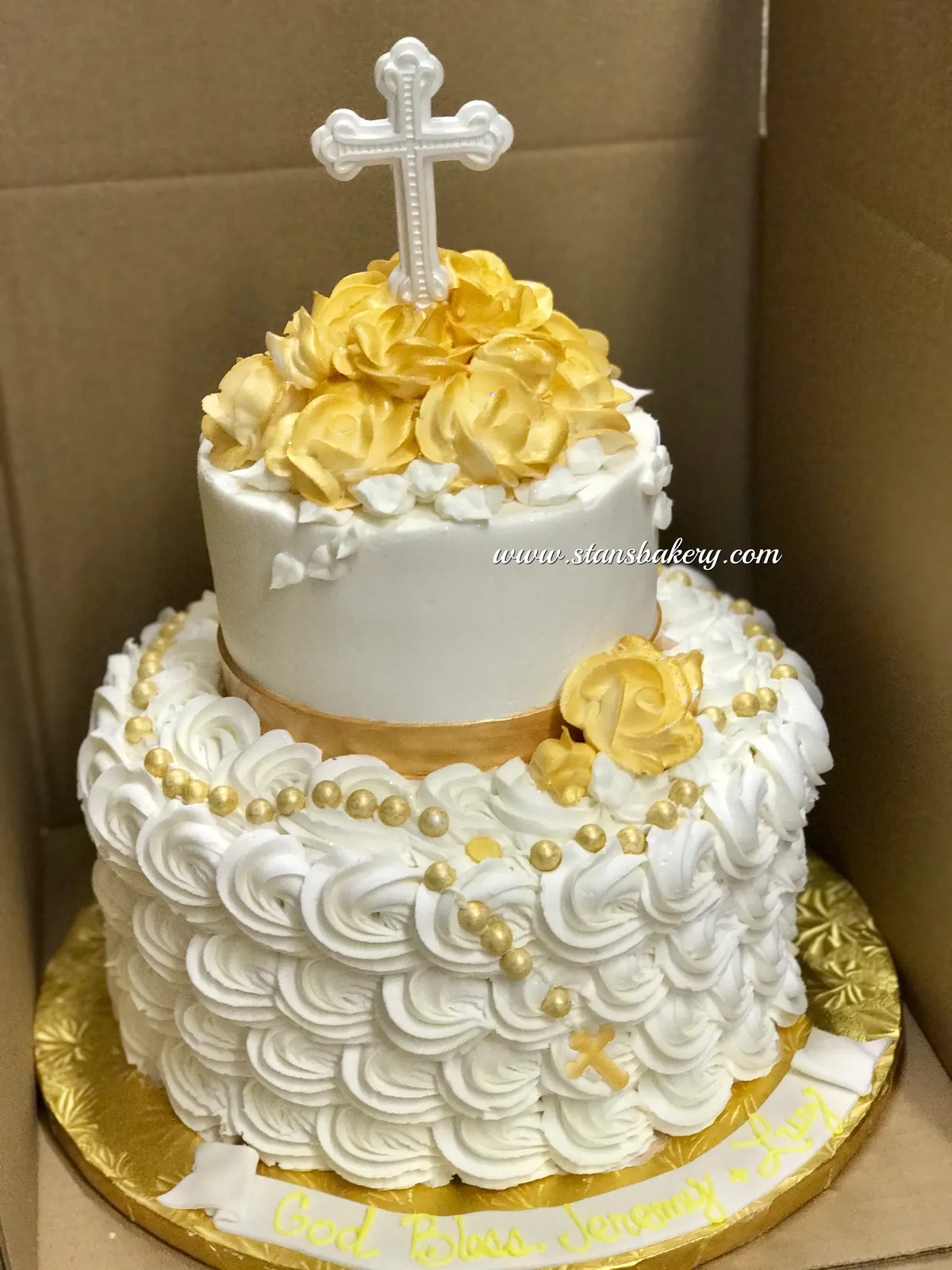 A white cake with gold roses and a cross topper