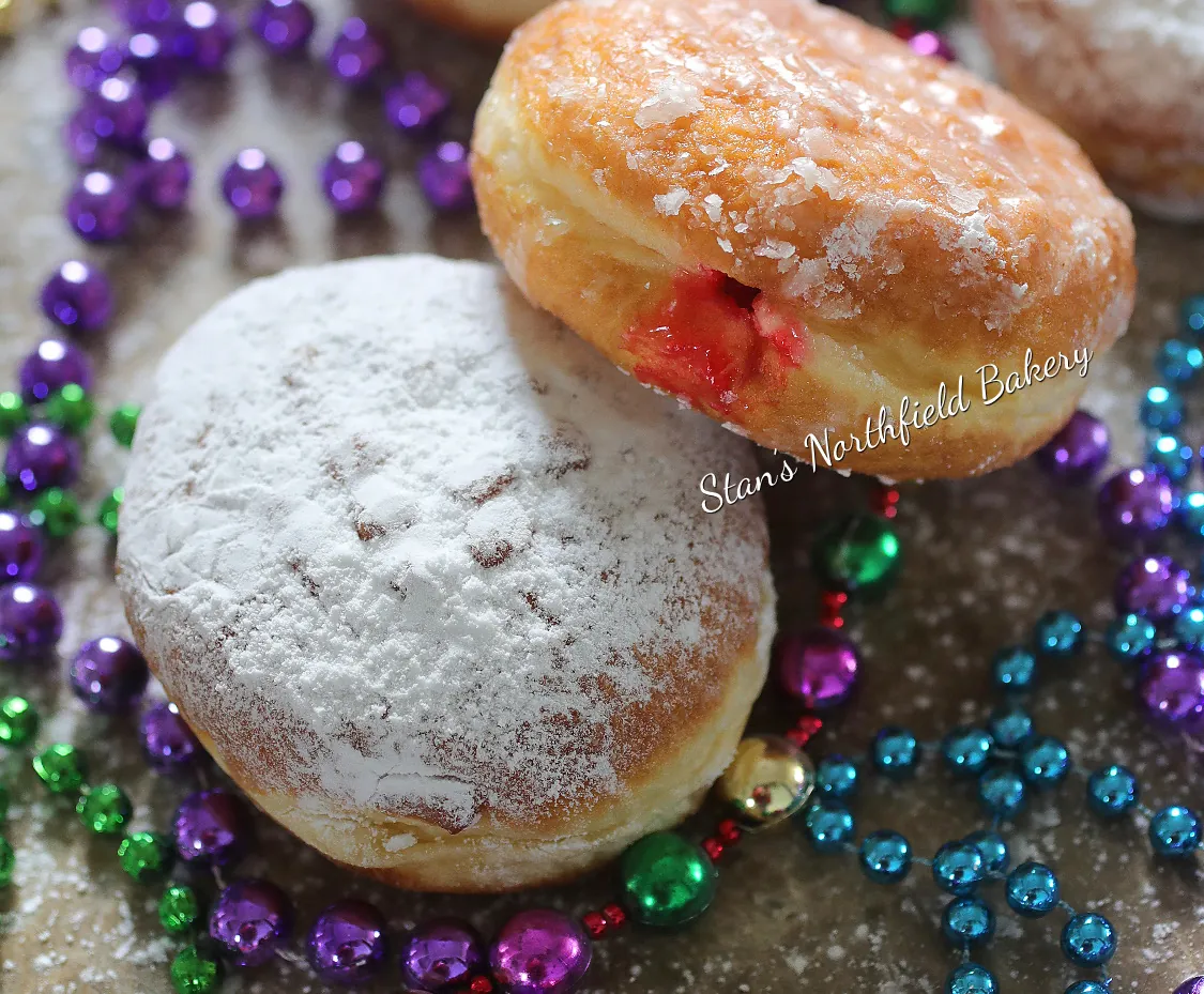 Powdered and glazed pączki with raspberry filling on Mardi Gras beads