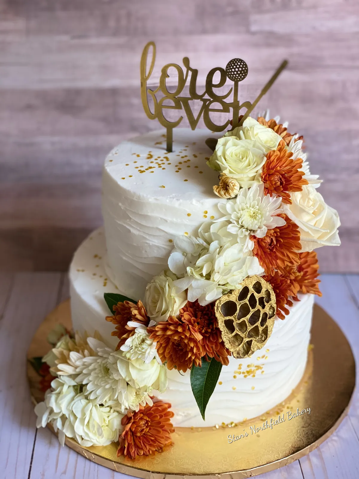A white cake with autumn flowers and a love topper