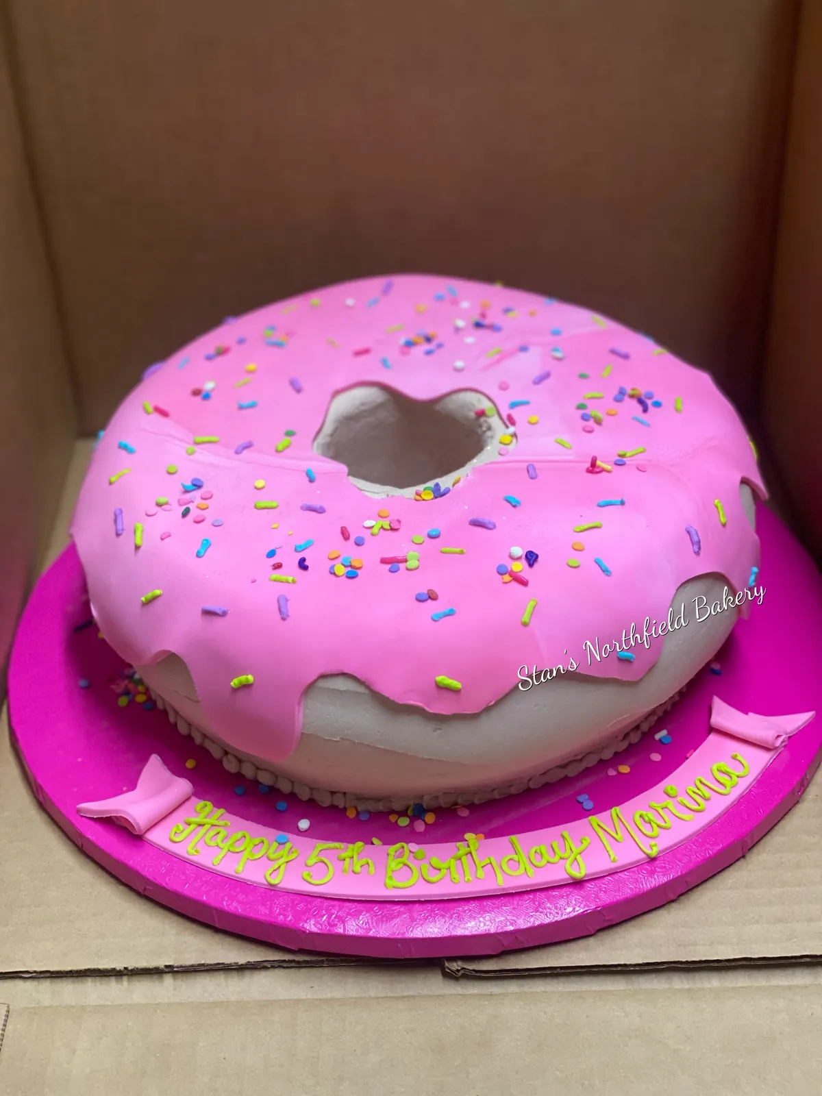 A cake shaped and iced as a giant pink sprinkle donut