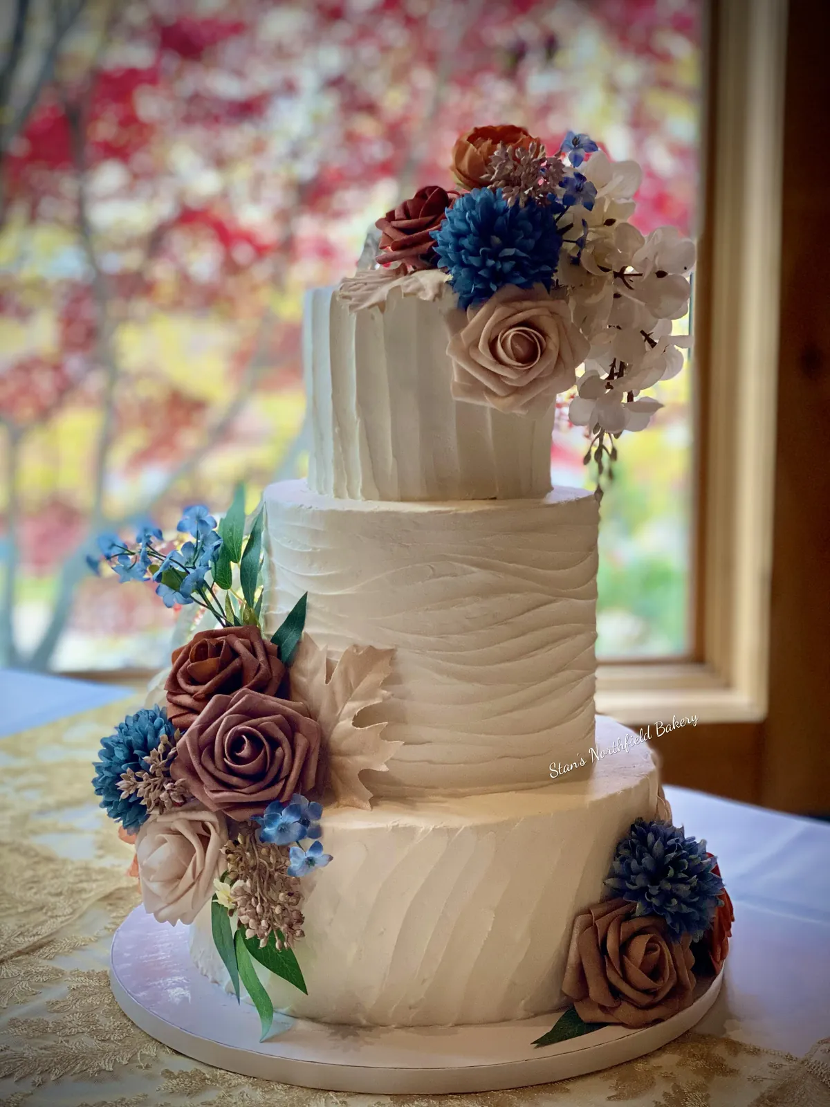 A three-tier textured buttercream cake with dusty rose, cream and navy sugar flowers