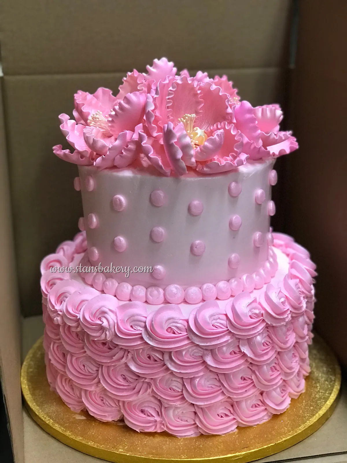 A pink two-tier cake with rosettes and ruffled flowers