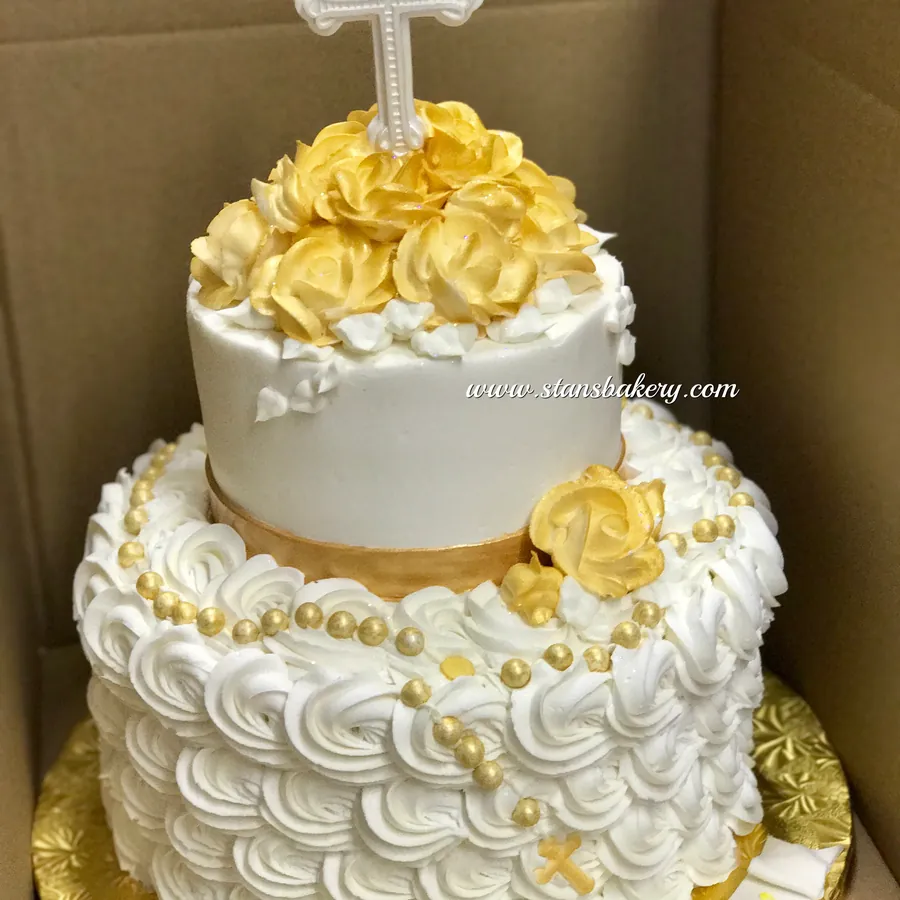 A white cake with gold roses and a cross topper