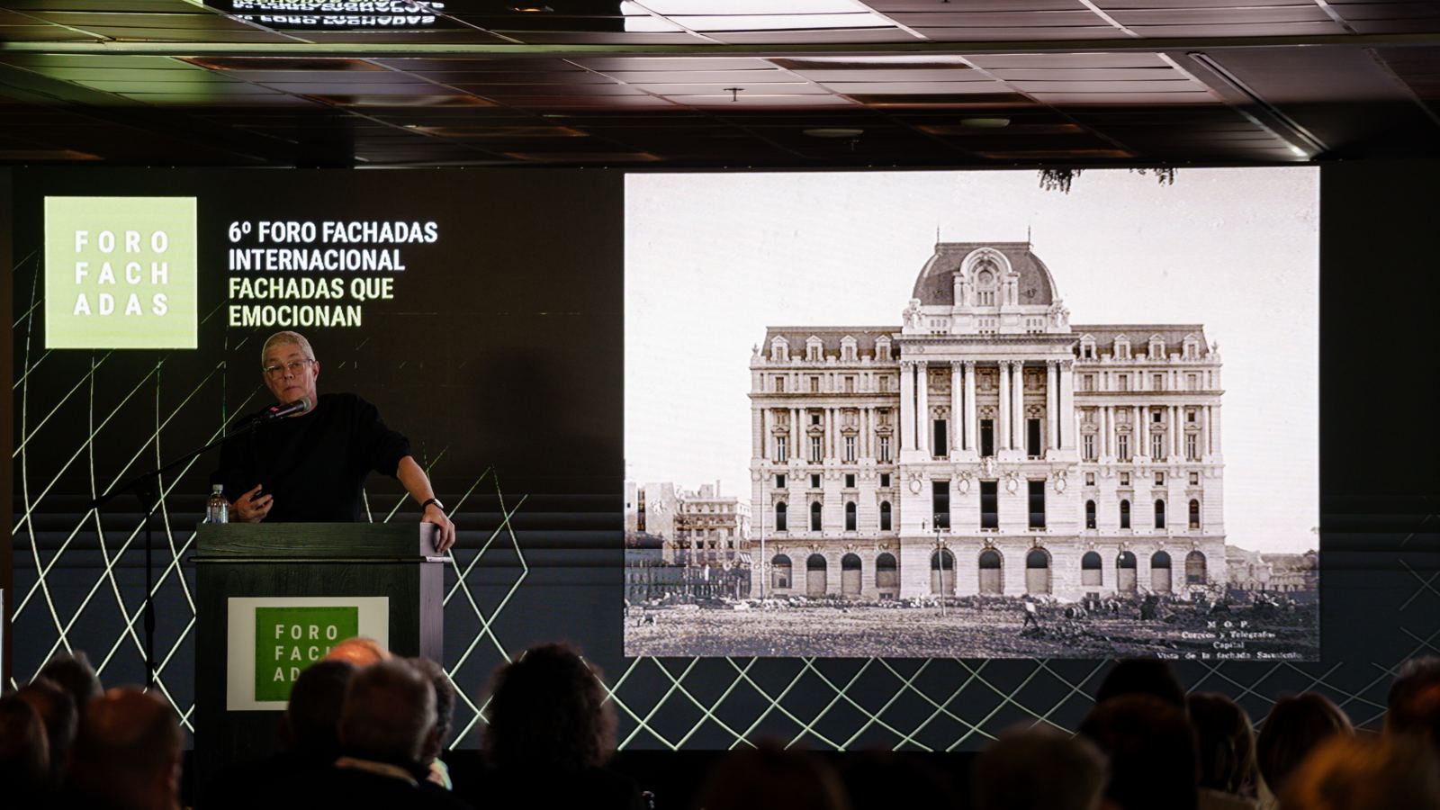 Orador en el atril del Foro de Fachadas con una imagen histórica del Palacio de Correos proyectada
