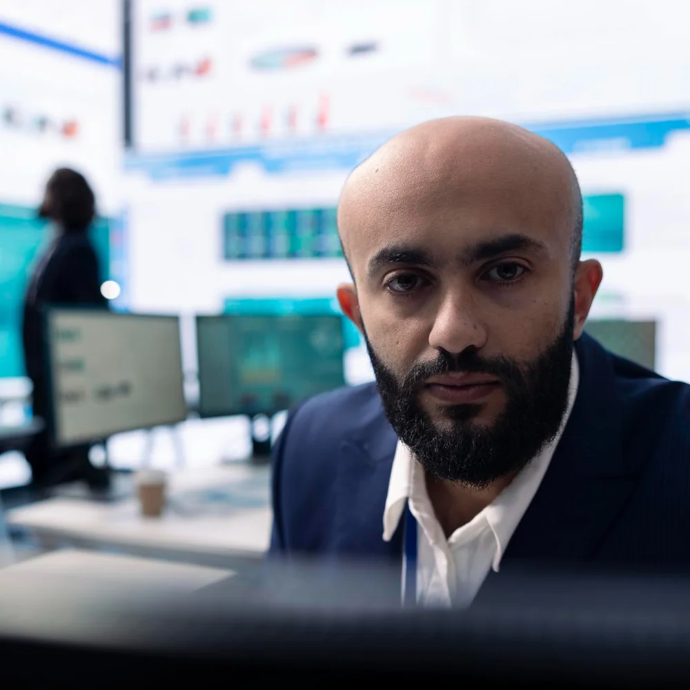 Man in office looking at camera with market information in background