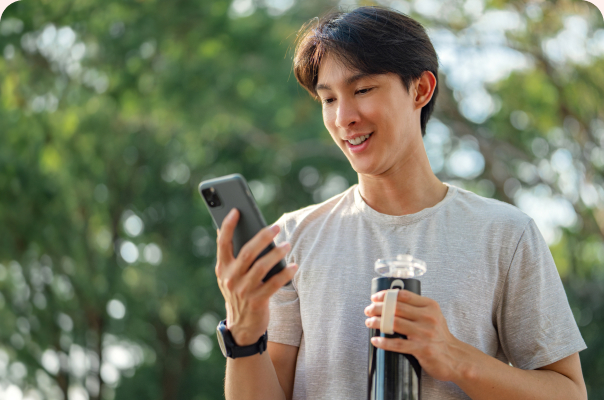 Young man smiling at his phone while holding a water bottle outdoors