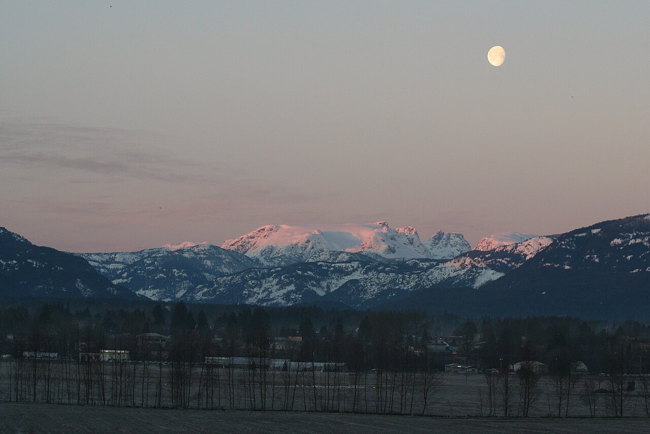 Snow-covered Comox Glacier above the Comox Valley at dawn, with the moon in the sky.