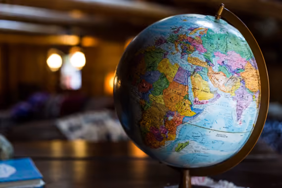 A colorful globe showing continents including Africa, Europe, and Asia, placed on a wooden surface with a blurred indoor background with warm lighting.