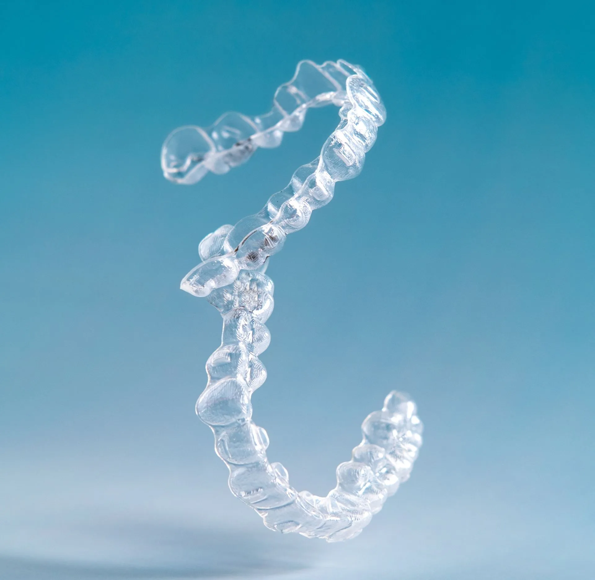 Clear Invisalign aligner tray floating against a blue background