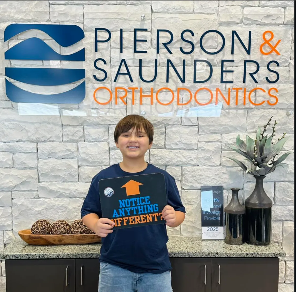 Young patient holding a 'Notice anything different?' sign at Pierson & Saunders Orthodontics