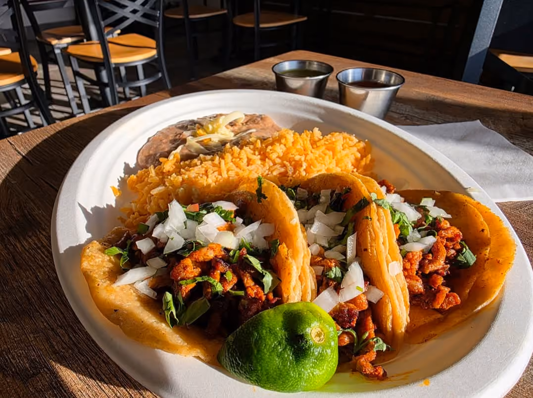 Tacos al pastor topped with onion and cilantro, served with a lime wedge